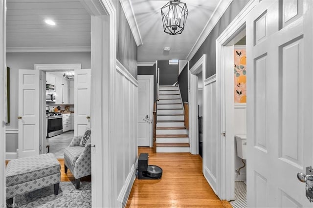 entrance foyer featuring light wood-type flooring, ornamental molding, stairway, a chandelier, and a decorative wall