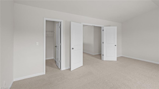 unfurnished bedroom with a walk in closet, baseboards, light carpet, and a closet
