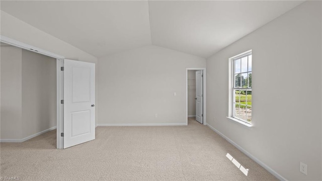 unfurnished bedroom with a closet, lofted ceiling, light carpet, baseboards, and a spacious closet