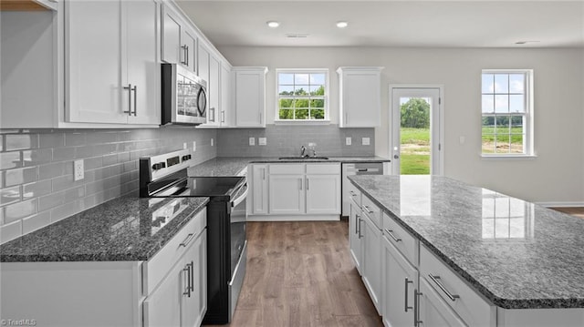 kitchen featuring a kitchen island, wood finished floors, a sink, stainless steel appliances, and white cabinetry