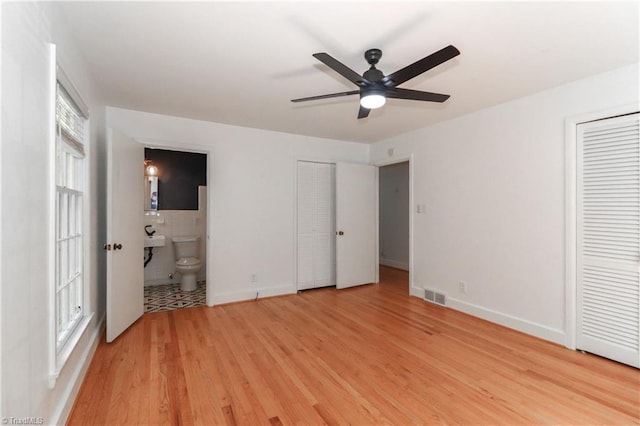 unfurnished bedroom featuring multiple closets, ensuite bathroom, ceiling fan, and light hardwood / wood-style floors