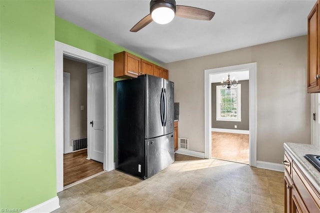 kitchen featuring brown cabinets, freestanding refrigerator, ceiling fan with notable chandelier, and visible vents