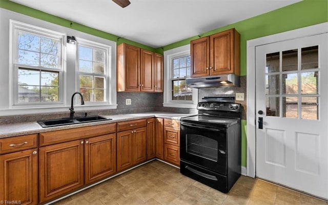 kitchen featuring brown cabinetry, under cabinet range hood, a sink, black electric range oven, and decorative backsplash