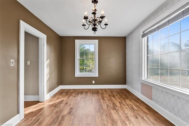 unfurnished dining area with a notable chandelier, baseboards, and wood finished floors