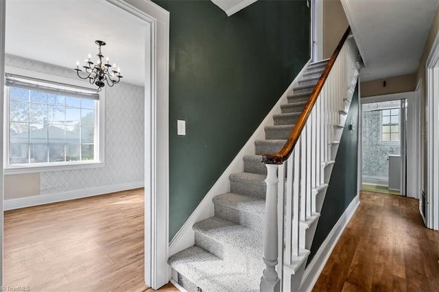 staircase featuring baseboards, a chandelier, wood finished floors, and wallpapered walls