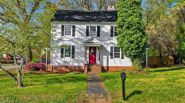 colonial home featuring a chimney, a front yard, and fence
