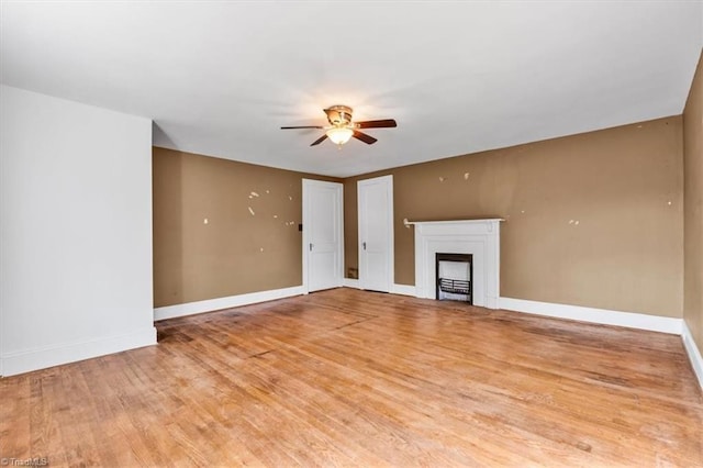 unfurnished living room with baseboards, a ceiling fan, a fireplace, and light wood finished floors
