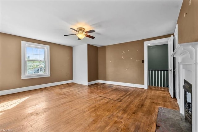 unfurnished living room with a brick fireplace, baseboards, wood finished floors, and ceiling fan