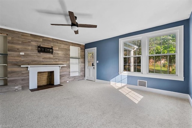 unfurnished living room featuring an accent wall, a ceiling fan, visible vents, wooden walls, and baseboards