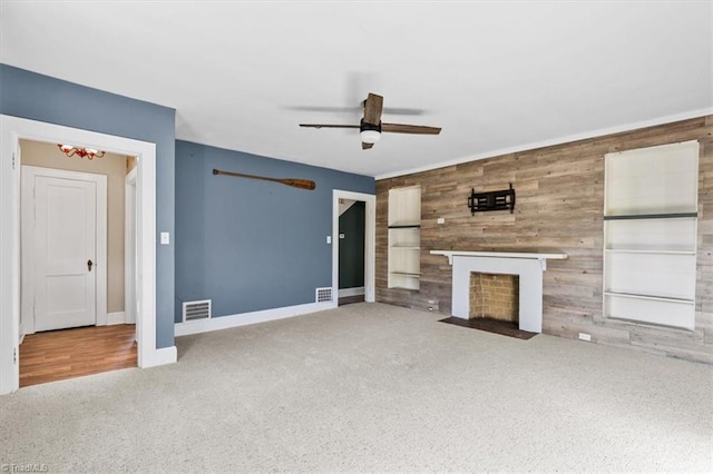 unfurnished living room with visible vents, an accent wall, carpet, a fireplace with flush hearth, and wood walls