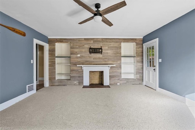 unfurnished living room with ceiling fan, carpet, a fireplace with flush hearth, an accent wall, and visible vents