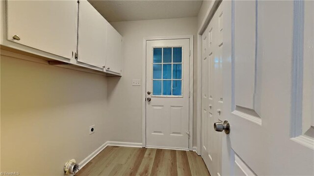 clothes washing area with electric dryer hookup, cabinet space, baseboards, and light wood finished floors