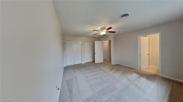 unfurnished bedroom featuring baseboards, multiple closets, visible vents, and carpet flooring