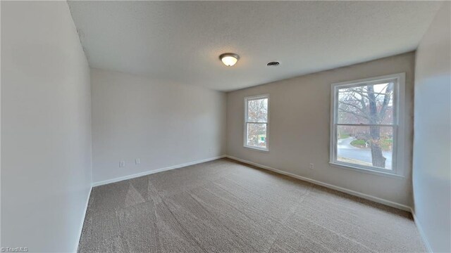carpeted spare room with baseboards, visible vents, and a textured ceiling