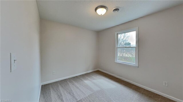 spare room with carpet floors, a textured ceiling, baseboards, and visible vents