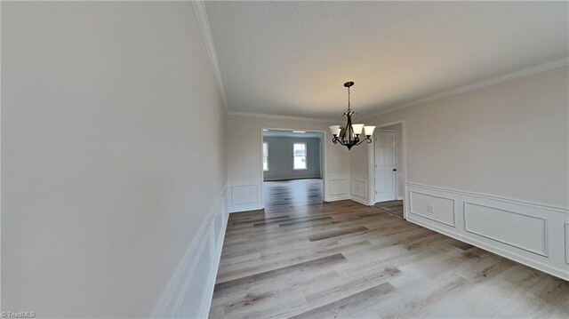 unfurnished dining area with crown molding, a chandelier, a wainscoted wall, light wood-style floors, and a decorative wall