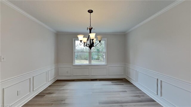 unfurnished dining area with a wainscoted wall, a notable chandelier, crown molding, and light wood-style flooring