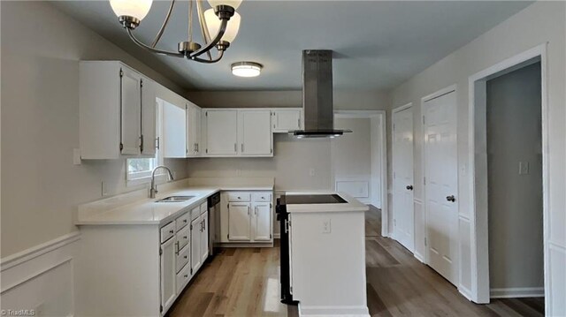 kitchen featuring dishwasher, white cabinetry, a sink, island range hood, and a notable chandelier