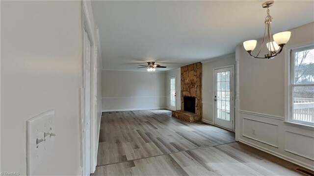 interior space featuring a stone fireplace, wainscoting, light wood-style flooring, ceiling fan with notable chandelier, and visible vents