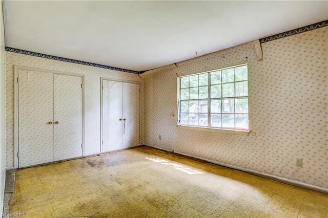 unfurnished bedroom featuring tile patterned floors, wallpapered walls, and multiple closets