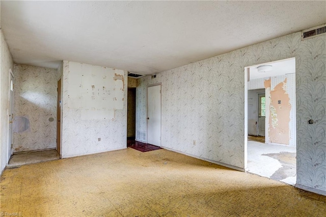 unfurnished room featuring tile patterned floors, visible vents, and wallpapered walls