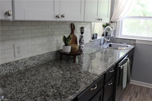 kitchen with a sink, wood finished floors, light stone counters, backsplash, and white cabinets