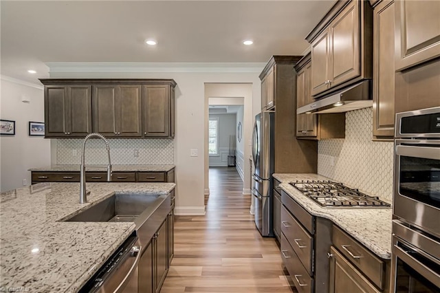 3609 Wesley Point Dr, Browns Summit, NC 27214 - kitchen with appliances with stainless steel finishes, under cabinet range hood, crown molding, light wood finished floors, and light stone countertops
