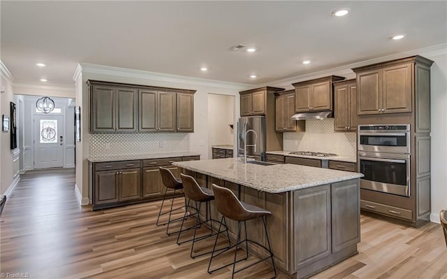 3609 Wesley Point Dr, Browns Summit, NC 27214 - kitchen featuring crown molding, appliances with stainless steel finishes, under cabinet range hood, light wood-style floors, and a breakfast bar area