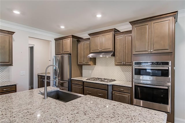 3609 Wesley Point Dr, Browns Summit, NC 27214 - kitchen featuring appliances with stainless steel finishes, under cabinet range hood, light stone counters, ornamental molding, and backsplash