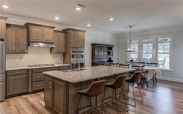 3609 Wesley Point Dr, Browns Summit, NC 27214 - kitchen with appliances with stainless steel finishes, under cabinet range hood, light wood-style flooring, ornamental molding, and light stone counters