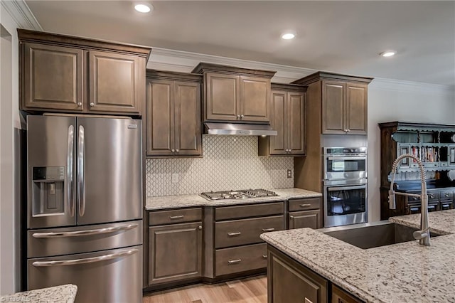 3609 Wesley Point Dr, Browns Summit, NC 27214 - kitchen with appliances with stainless steel finishes, crown molding, light stone counters, under cabinet range hood, and dark brown cabinetry