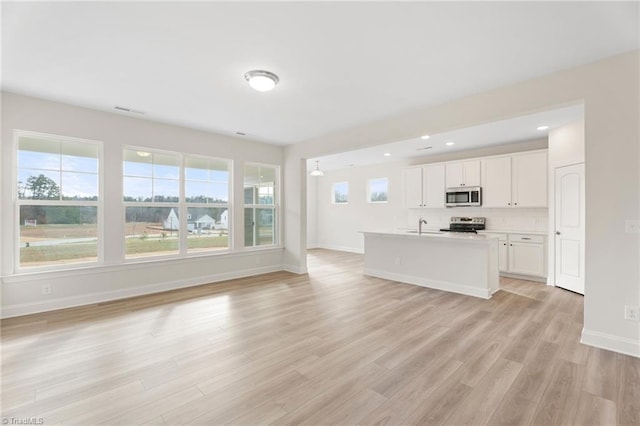 kitchen with a kitchen island with sink, light wood-type flooring, appliances with stainless steel finishes, tasteful backsplash, and white cabinetry