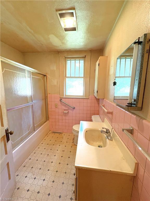 200 N 9th Ave, Mayodan, NC 27027 - bathroom with tile walls, vanity, tile patterned floors, combined bath / shower with glass door, and a textured ceiling
