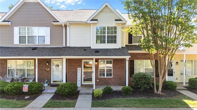 multi unit property with brick siding, a porch, and roof with shingles