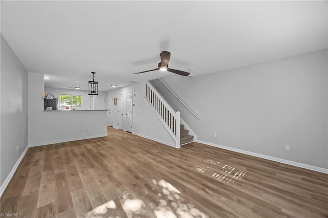 unfurnished living room featuring baseboards, stairway, wood finished floors, and a ceiling fan