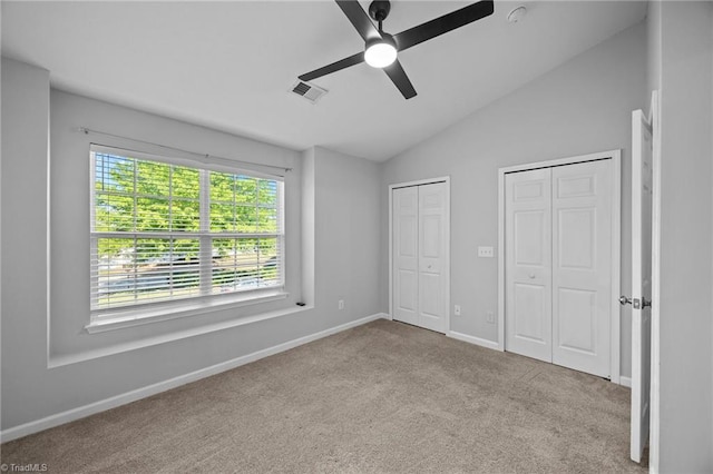 unfurnished bedroom featuring multiple closets, carpet floors, vaulted ceiling, baseboards, and ceiling fan