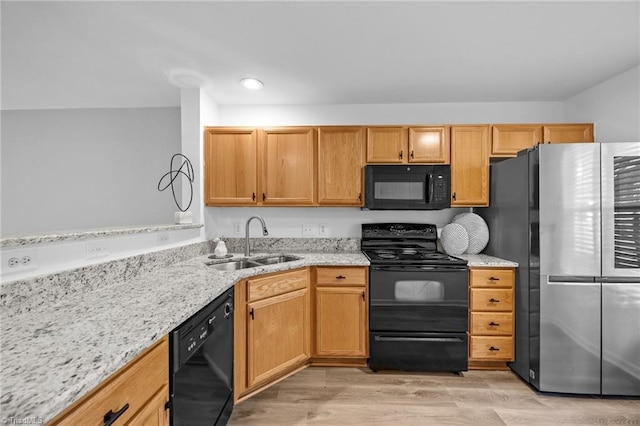 kitchen featuring black appliances, a sink, light stone countertops, light wood-style floors, and recessed lighting