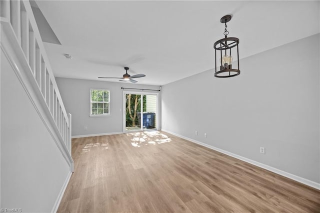 unfurnished living room with light wood-style floors, baseboards, stairs, and a ceiling fan