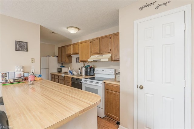 kitchen with light countertops, brown cabinetry, a textured ceiling, white appliances, and under cabinet range hood