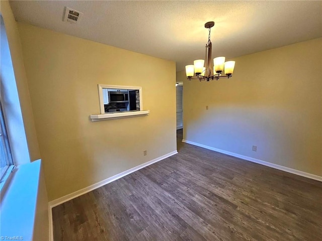 spare room featuring a textured ceiling, a chandelier, and dark hardwood / wood-style flooring