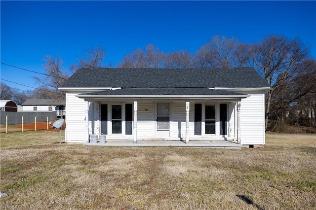 exterior space featuring covered porch, a front lawn, roof with shingles, and fence