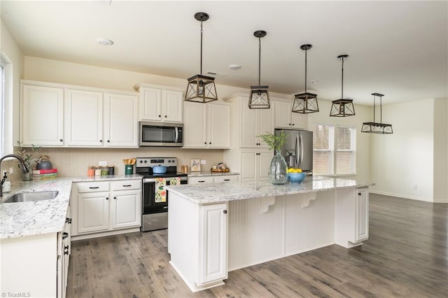 kitchen with pendant lighting, sink, stainless steel appliances, white cabinets, and a kitchen island