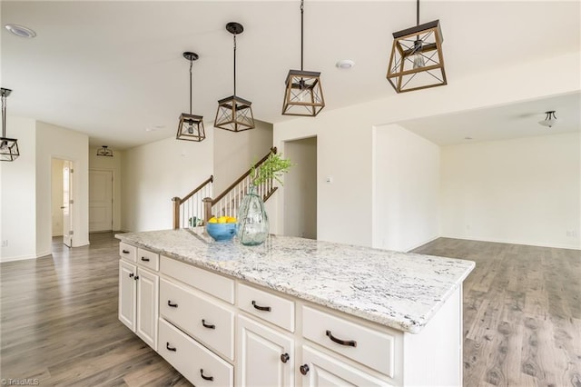 kitchen with pendant lighting, white cabinetry, light stone counters, wood-type flooring, and a kitchen island