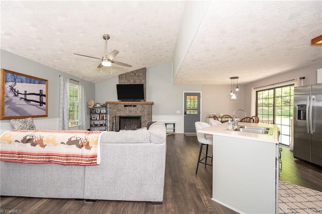 living area with a stone fireplace, a textured ceiling, ceiling fan, and dark wood-style flooring
