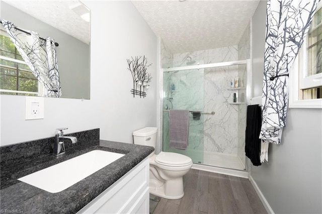 bathroom featuring a textured ceiling, wood finished floors, vanity, toilet, and a marble finish shower