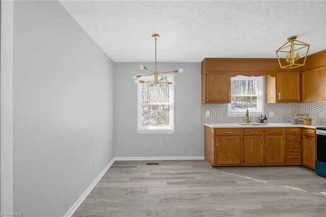 kitchen with sink, backsplash, stainless steel range with electric stovetop, pendant lighting, and a notable chandelier