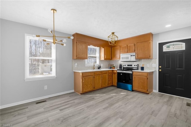 kitchen featuring a wealth of natural light, hanging light fixtures, a notable chandelier, light wood-type flooring, and stainless steel electric range oven