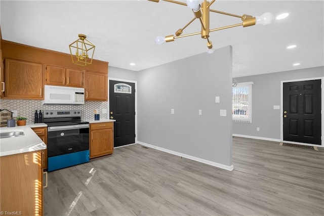 kitchen with electric range, light wood-type flooring, pendant lighting, and decorative backsplash