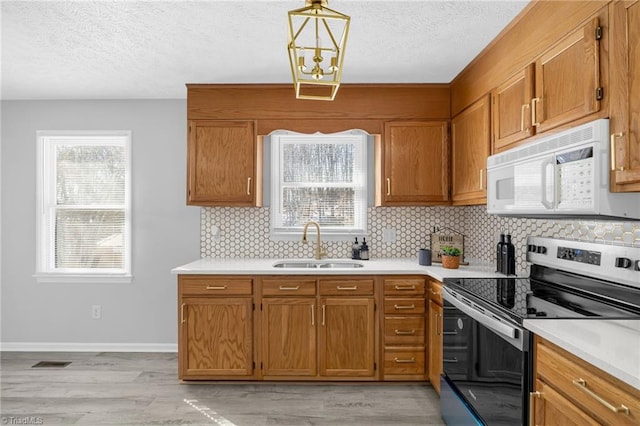 kitchen with light wood-type flooring, pendant lighting, stainless steel range with electric stovetop, decorative backsplash, and sink