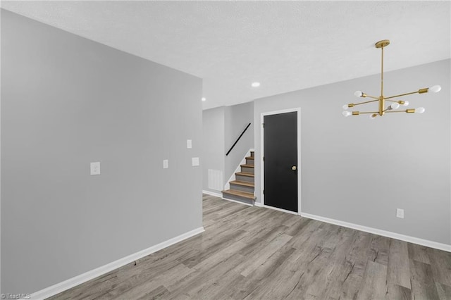 spare room with a notable chandelier and light wood-type flooring